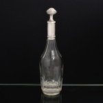 PRATA FRANCESA E CRISTAL, uma (1) antiga garrafa licoreira, lapidação dita dedão, manufatura CRISTALERIE BACCARAT (fundada em 1765 pelo Bispo de Metz na região de Baccarat como Verrerie de Saint Anne; em 1815 foi vendida, junto com outras Verreries da região, para Gabriel D'Artigues e virou Voneche-Baccarat, passando a fabricar cristal de alta qualidade; em 1822 foi vendida e virou Compagnie des Cristalleries de Baccarat, mantendo o nome Voneche até 1843, atualmente é a Cristallerie mais importante da França), monture canelado com os seguintes punções: HL (ourives Henry Lapeyre, ativo entre 1895 e 1923, estabelecido à época na Rue Meslay  Paris); Tete de Mercury (garantia do teor da prata 950 milésimos), possui mossas, peso aproximado somente da prata 100 gr., medindo 31,5 cm altura, vide foto.