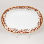 PORCELANA, uma (1) travessa ovalada de borda alta, ornada com faixa marrom e barrado vegetalista, arremates com frisos a ouro, modelo MON CHERI, marca RENNER (Porto Alegre, RS, fundada em 1942; em 1998 foi vendida para a Vista Alegre de Portugal; em 1999 mudou a razão social para Vista Alegre do Brasil), medindo 23 x 15,5 x 4 cm, vide foto.