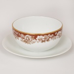 PORCELANA, uma (1) molheira com presentoir, ornada com faixa marrom e barrado vegetalista, arremates com frisos a ouro, modelo MON CHERI, marca RENNER (Porto Alegre, RS, fundada em 1942; em 1998 foi vendida para a Vista Alegre de Portugal; em 1999 mudou a razão social para Vista Alegre do Brasil), medindo 18 cm diâmetro, vide foto.