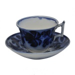 Xicara com seu pires em louça inglesa decorado com o clássico padrão azul borrão (flow blue) de motivos florais difusos. Fundo com craquele. 6.5 x 8.5 cm / 14 cm (pires).