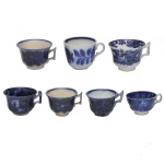 Conjunto de 7 xícaras SEM pires em louça decoradas com o clássico padrão azul borrão (flow blue) de motivos florais difusos .8 x 8 cm maior / 5 x 7 cm menor. Apresenta sinais de uso e do tempo.