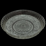 Prato para bolo em cristal, de formato circular fundo, com borda levemente revirada e decorada por gomos. Fundo moldado, profusamente ornado por rosácea com volutas e flores de lis alternadas, centralizando medalhão com facetas em bico de jaca e adorno estrelar ao centro. 6 x 30 cm.