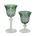 Conjunto de 2 belos taças em cristal da Boêmia, decorados em overlay verde esmeralda, de feitio idêntico mas de tamanhos distintos. Bojos fundos com bordas reviradas, lapidados e ornamentados por arcos, treliças em reservas e raiados. Hastes retas e facetadas, interrompidas por anelados salientes, apoiadas em pés moldados com gomos em leque.16 cm e 12 cm.