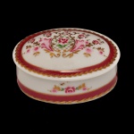 Caixa porta joias vintage em porcelana Royal Porcelain P. Limoges, pintada à mão. Acabamento em porcelana branca decorado com delicados motivos florais de rosas, detalhes e arabescos em dourado, além de uma marcante faixa decorativa na cor vermelho bordeaux. Apresenta a inscrição manuscrita "P. Limoges", associada a peças de porcelana decorativas inspiradas ou provenientes da tradição de Limoges, na França. A indicação "24 KT Gold" aponta que a peça possui detalhes ou acabamento em ouro de 24 quilates. 3 x 6 cm.