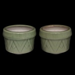 Par de cachepots em porcelana chinesa, revestidos por cobertas celadon de cor verde água. Bojos cilíndricos ornados por frisos triangulares e encimados por bordas salientes com gregas. China. Séc. XX. 8 x 11 cm.