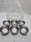 Lote de travessa redonda em demicristal ricamente trabalhado com 6 cumbucas de sobremesa em aço inox. Medindo a travessa 31cm x 6cm de altura e as cumbucas 9cm x 5cm de altura.