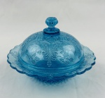 Manteigueira de coleção em vidro na cor azul, decoração em relevo, com flores e motivos geométricos, bordas recortadas e fundo estrelar. Medindo: 12 x 17 cm. 