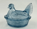 Manteigueira de coleção em vidro na cor azul, representando galinha em ninho, decoração em relevo. Medindo: 12 x 13 x 10 cm.