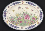 China. Travessa em Porcelana chinesa esmaltados com rica decoração policroma de motivos florais, folhagens e borboletas; detalhes em azul e bordô ao gosto Famille Rose. Marcado ao fundo em azul. Medindo: 40,5 x 30 cm.