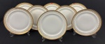 Limoges, France. Oito pratos rasos em porcelana esmaltada na cor branca com rica decoração em douração, composta por faixa ornamental de inspiração neoclássica, formada por reservas ovais com motivos florais estilizados, folhagens e arabescos, dispostos em composição rítmica e simétrica. Apresenta frisos e filetes concêntricos em ouro, acabamento de grande elegância e requinte. Manufatura no verso. Medindo: 24 cm.  Apresentam desgastes e 2 com bicado.