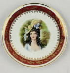 Schmidt - Prato em porcelana na cor branca, esmaltado com dama ao centro, listra no tom vermelho, ricos detalhares e filetes dourados. Marcado ` By Joh Peters, Amsterdam - Holland `. Medindo: 26 cm. Apresenta fio de cabelo.