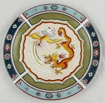 Prato decorativo em porcelana chinesa, apresenta ao centro rica composição policromada com dragão e fênix. Borda ornamentada com motivos florais, escamas estilizadas em tons de azul, vermelho, dourado, branco e verde. Medindo: 25 cm.