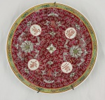 Prato decorativo em porcelana chinesa, com decoração policromada em fundo rosa com flores, folhagens e ornamentos estilizados, além de quatro reservas circulares contendo caracteres chineses. Bordas ornamentadas com gregas sobre fundo amarelo. Acompanha suporte de parede. Medindo: 25 cm.