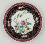 Prato decorativo em porcelana chinesa com decoração policroma de flores, árvore e pássaros. Bordas em tons de preto, vermelho, azul e amarelo, ornamentando com flores, arabescos e elementos geométricos. Medindo: 26 cm.