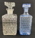 Duas licoreiras em vidro lapidado, sendo uma translúcida e outra azul. Medindo: 23 cm e 22 cm. Azul com lascas na tampa interna.