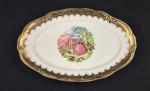 Travessa oval em porcelana esmaltada, borda com rica decoração em ouro e parte central com cena galante policroma. Medindo: 41 x 26 cm.