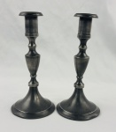 Par de castiçais em estanho, com hastes torneadas e ornamentadas, apresentando corpo de formato elegante e bases circulares amplas. Altura: 19 cm.