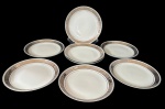 Steatita - Oito pratos para sobremesa em porcelana com aba decorada em tom prateado e detalhes em relevo formando cenas clássicas ao redor da borda. Filete fino próximo à área central. Medindo: 19 cm.