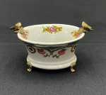 Artcurial e Peça de Limoges. Pequeno centro de mesa ou cachepot decorativo em porcelana francesa de Limoges com  guirlanda floral e trançado dourado e delicada pintura floral no interior tendo duas borboletas  em bronze encimadas na borda e 4 pés em formato de garra em bronze. Possui no verso marca geométrica abstrada policromada que corresponde a  assinatura institucional da Artcurial e foi desenhado para  servir de selo editorial da galeria francesa em suas parcerias artísticas no início da década de 1970, ano em que a famosa editora de arte parisiense lançou edições limitadas de objetos de arte e porcelana de Limoges sendo a marca o design e formas circulares justapostas da série Rythmes de Sonia e Robert Delaunay. Medindo: 10 x 11 x 18 cm.