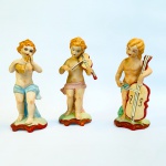 Três estatuetas produzidas em biscuit policromado representando querubins (anjos músicos). Med 17 cm. 