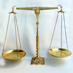 Grande e imponente balança decorativa toda em metal amarelo polido com dois pratos, base quadrangular ricamente ornamentada em alto relevo. Med 52 cm x e 62 cm. 