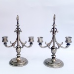 Par de castiçais para duas velas confeccionados em metal branco. Base redonda em gomos, haste decorada, braços em volutas e pega circular. Med 23cm alt x 20cm larg.