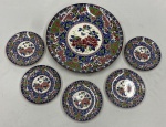 Grande prato de porcelana japonesa no estilo Imeri, tradicionalmente originário em regiões como  Arita, famosa por sua paleta de cores vibrantes  O design apresenta uma rica decoração floral policromática detalhada com uma medalhão central branco decorado com borboletas e peônias cercada por ricas faixas geométricas e florais repetidas nas bordas.  São peças produzidas por renomadas olarias da região. Marcado na base. Acompanham 5 pratinhos no mesmo padrão. Medindo: 3,5 x 32 cm e 15 cm.