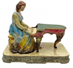 Antiga e grande estatueta de porcelana portuguesa policromada com extrema riqueza de detalhes, da marca TASCA, representando dama de época  com vestes clássicas tocando um piano de cauda. Medindo: 32 x 36 x 17 cm.