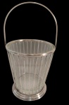 CHRISTOFLE. Balde de gelo com recipiente em vidro translúcido, envolvido por estrutura vazada em metal espessurado a prata, formada por hastes verticais, aro superior liso, alça móvel arqueada e base circular moldurada. Marca do fabricante na estrutura. Medindo: 25 x 14 cm.