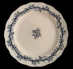BWM & Co. Inglaterra. Antigo prato em faiança, padrão `Lobelia`, com decoração floral em azul sobre fundo marfim, ramalhete no centro e cercadura de flores e fitas na aba, borda de contorno ondulado. Marca no verso. Apresenta craquelê, amarelamento e marcas do tempo. Medindo: 30 cm de diâmetro.