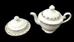 REAL. Conjunto de duas peças em porcelana nacional branca, composto por bule com tampa e manteigueira com tampa, decorados com pequenas rosas, folhagens e filetes dourados. Bule com corpo bojudo, bico alongado e alça curva; manteigueira com borda levemente recortada. Marca do fabricante na base. Medidas: bule, 22,3 x 13,3 x 15 cm; manteigueira, 15 x 9 cm.