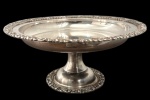 Antiga fruteira em metal espessurado a prata, com recipiente circular sobre pedestal e base redonda. Borda e base decorados com motivos florais e volutas em relevo. Medidas: 15 cm de altura x 36,6 cm de diâmetro.