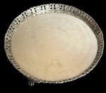 Bandeja / salva circular em metal espessurado a prata, com centro gravado com guirlandas de folhagens e faixas concêntricas onduladas. Borda elevada, recortada e vazada, decorada com motivos vegetalistas e volutas em relevo, sobre pequenos pés trabalhados. Marcas de uso na superfície. Medidas: 5 cm de altura x 31,5 cm de diâmetro.