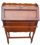 Escrivaninha moderna tipo secretaire em madeira, com tampo frontal rebatível e moldurado, interior com três pequenas gavetas e duas gavetas externas com puxadores torneados. Prateleira superior com espaldar recortado, pernas torneadas unidas por travessas e espelho de fechadura em metal. Apresenta riscos e desgaste no acabamento. Medidas: 102 x 80 x 37 cm.
