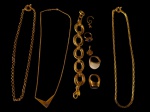 Bijuteria vintage em metal dourado, composto por três colares de diferentes malhas, um deles com adorno geométrico em `V`; um bracelete de elos ovais com detalhes torcidos; três anéis de modelos variados, com elementos nas cores azul, creme e preta; e dois pingentes, sendo um espiralado e outro em formato de trevo. Total de 9 peças.
