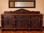 Imponente buffet em madeira entalhada, com duas portas laterais e três gavetas centrais, ricamente decorado com cabeças de leão, volutas, folhagens e concheados em relevo. Tampo retangular com borda moldurada, espaldar recortado e pés torneados. Medidas: 100 x 210 x 75 cm. Acompanha espelho.