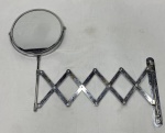 Espelho de parede em metal cromado, com moldura circular basculante e braço articulado extensível em sanfona.  Medidas: 35 x 9 cm fechado; extensão de 50 cm. Apresenta pontos de oxidação e desgastes no cromado.