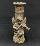 Castiçal em resina com acabamento dourado e pátina, ornamentado com anjo tocando violino, coluna canelada e base com volutas em relevo. Apresenta desgaste no acabamento. Medidas: 17 x 7 x 7 cm.