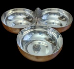 Christofle. Petisqueira tripla da prestigiada manufatura francesa em metal espessurado a prata, composta por três bowls circulares, com acabamento liso e polido, artisticamente unidos ao centro por uma coluna cilíndrica canelada que serve de suporte para uma suntuosa e detalhada pega decorativa em formato de pinha (pomo) com folhas de acanto na base, marcas de punção da marca na parte inferior. Medidas: 9 x 23 x 21,5 cm