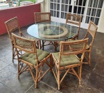 Conjunto de mesa redonda com 6 cadeiras, em estrutura de bambu/vime natural, tampo em vidro redondo. Mesa com 1,06 m de diâmetro, base central em estrutura trançada. Cadeiras com encosto e assento em trama natural, acompanhadas de almofadas estofadas na cor verde militar. Peça de estilo rústico tropical, ideal para varandas, áreas gourmet ou ambientes externos cobertos. Conjunto harmonioso, leve e decorativo. Lote composto por 1 mesa e 6 cadeiras. Apresenta marcas de uso e do sol.