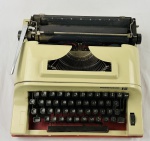 REMINGTON 15 - Máquina de escrever manual, com carenagem na cor creme, base vermelha, teclado preto e alavanca metálica de retorno do carro. Apresenta desgaste no acabamento e pontos de oxidação nas partes metálicas.