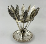 Conjunto de garfinhos para aperitivo em metal espessurado à prata, com cabos decorados em relevo com figuras, paisagens e inscrições alusivas a cidades brasileiras. Acompanha suporte circular com haste central e base moldurada. Apresenta oxidação e desgaste no prateamento.