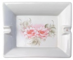 Cinzeiro para charutos em porcelana, formato retangular com apoios laterais para cigarro, decorado ao centro com pintura floral em delicados tons de rosa e verde. Peça esmaltada. Medidas: 19  15 cm. Estado compatível com o uso.