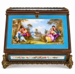 PORCELANA SÈVRES  Rarissima escrivaninha de viagem em porcelana de Sèvres, século XVIII, de formato arquitetônico, decorado em azul-celeste com reservas pintadas à mão com cenas galantes e delicados motivos florais, enriquecido por molduras em madeira e aplicações ornamentais em metal dourado. Peça de grande requinte decorativo, com ferragens, pés e ornamentos em estilo rococó. Mede 25,5 cm de altura x 35 cm de comprimento x 24 cm de largura.