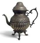 Bule em metal espessurado à prata, cerca de 1900, de corpo bojudo com decoração em relevo e pés ornamentais. Falta a pega da tampa. Desgaste do tempo. Mede 30 x 28 cm.