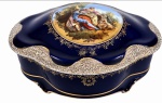 PORCELANA EUROPEIA, século XIX. Rara caixa com tampa em porcelana de intenso azul-cobalto, decoração dourada e aplicações ornamentais em relevo, apresentando ao centro delicada cena galante/pastoral pintada à mão. Interior em porcelana branca. Peça de elegante padrão decorativo e caráter ornamental. Ideal para colecionadores de bom gosto.Medidas: 28 x 20 cm.