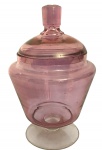 Bombonière em vidro rosado com tampa, formato clássico sobre base elevada. Peça delicada e decorativa. Possui discreto bicado na borda interna. Mede 24cm altura.