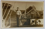 Foto Época (1946) Jovem no Convés de Navio a Vapor  Papel Ferrania Antigo Interessante registro histórico e náutico em preto e branco. A imagem mostra um jovem bem trajado à moda dos anos 1940 (camisa clara com mangas dobradas e calça de alfaiataria de cós alto com pregas) posando no convés superior de uma embarcação em alto-mar. Há ricos detalhes técnicos do navio visíveis ao fundo, incluindo cabos de sustentação, escotilhas circulares, o que parecem ser botes ou balsas salva-vidas numeradas com estruturas metálicas de lançamento, e outros tripulantes ou passageiros abaixo.