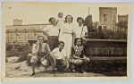 Foto Época (c. 1940/1950) Grupo Familiar em Chafariz com Arquitetura ao Fundo  Borda Canoa O grande diferencial deste lote são as vestimentas de época muito elegantes (incluindo óculos de sol marcantes e um chapéu de palha na mão de uma das integrantes) e a imponente arquitetura de tijolos com torres ameadas (estilo castelo/militar ou fabril antigo) ao fundo, o que pode ajudar pesquisadores a identificar a localidade exata do registro.