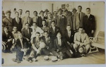 Foto Histórica Época (c. 1920/1930) Delegação ou Time de Futebol com Bola Antiga de Couro  Raro e imponente registro social masculino que captura cerca de 25 homens posando em grupo. O grande diferencial colecionável e ponto central deste lote é o rapaz sentado ao meio segurando uma bola de futebol antiga de couro com gomos (estilo T-shape ou clássica dos anos 20/30).